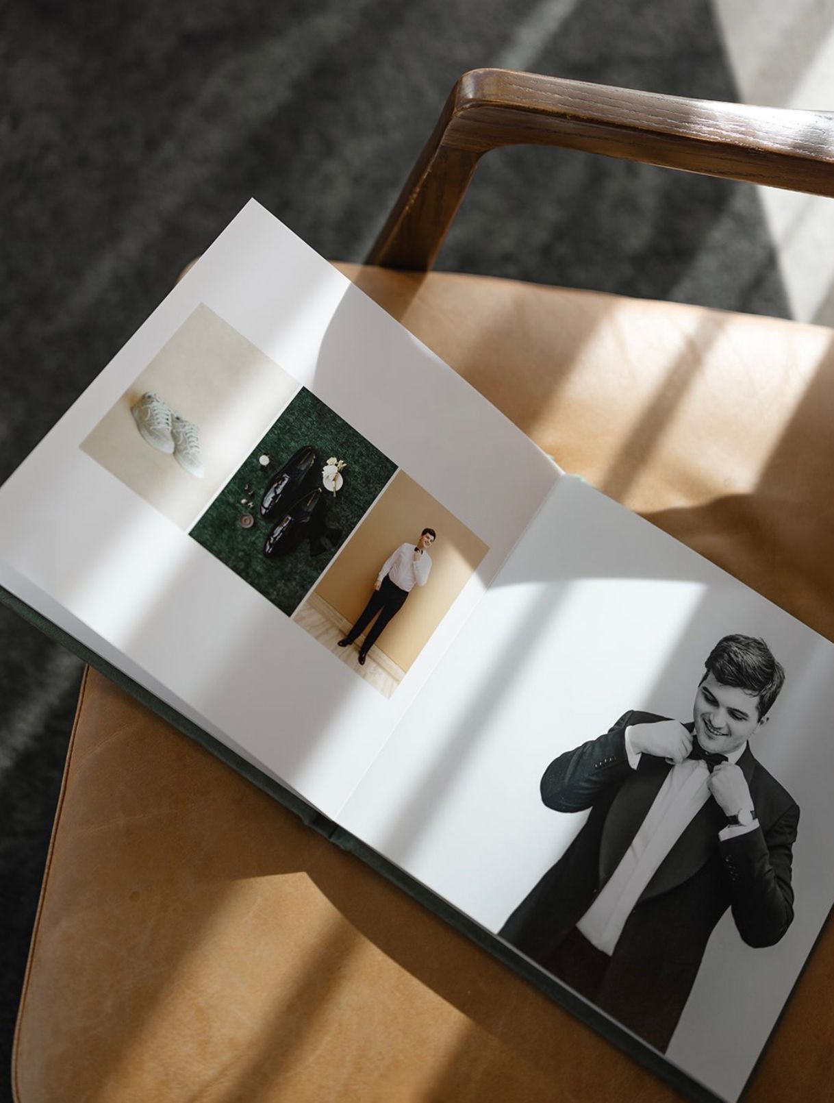 Open wedding photo album on wooden chair displaying elegant groom portraits in black suit, bathed in natural sunlight.