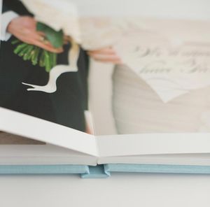 Open wedding photo album with blue spine showing bride holding bouquet and calligraphy vow card pages.