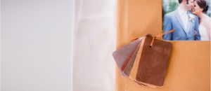 Leather wedding album swatches displayed on a tan surface beside a romantic couple portrait photo.