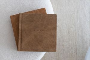 Two brown leather-bound photo albums stacked on a white textured surface with embossed text on the cover.