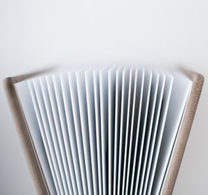 Close-up of an open book with fanned pages creating a symmetrical pattern against a white background.