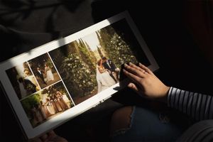 Person browsing a wedding photo album featuring elegant outdoor ceremony pictures of bride and groom.