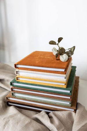 Stack of colorful hardcover books with a small eucalyptus branch on top, arranged on a linen cloth.