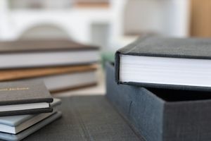 Stack of hardcover books and journals on a table, with a gray linen-bound book in a matching slipcase in focus.