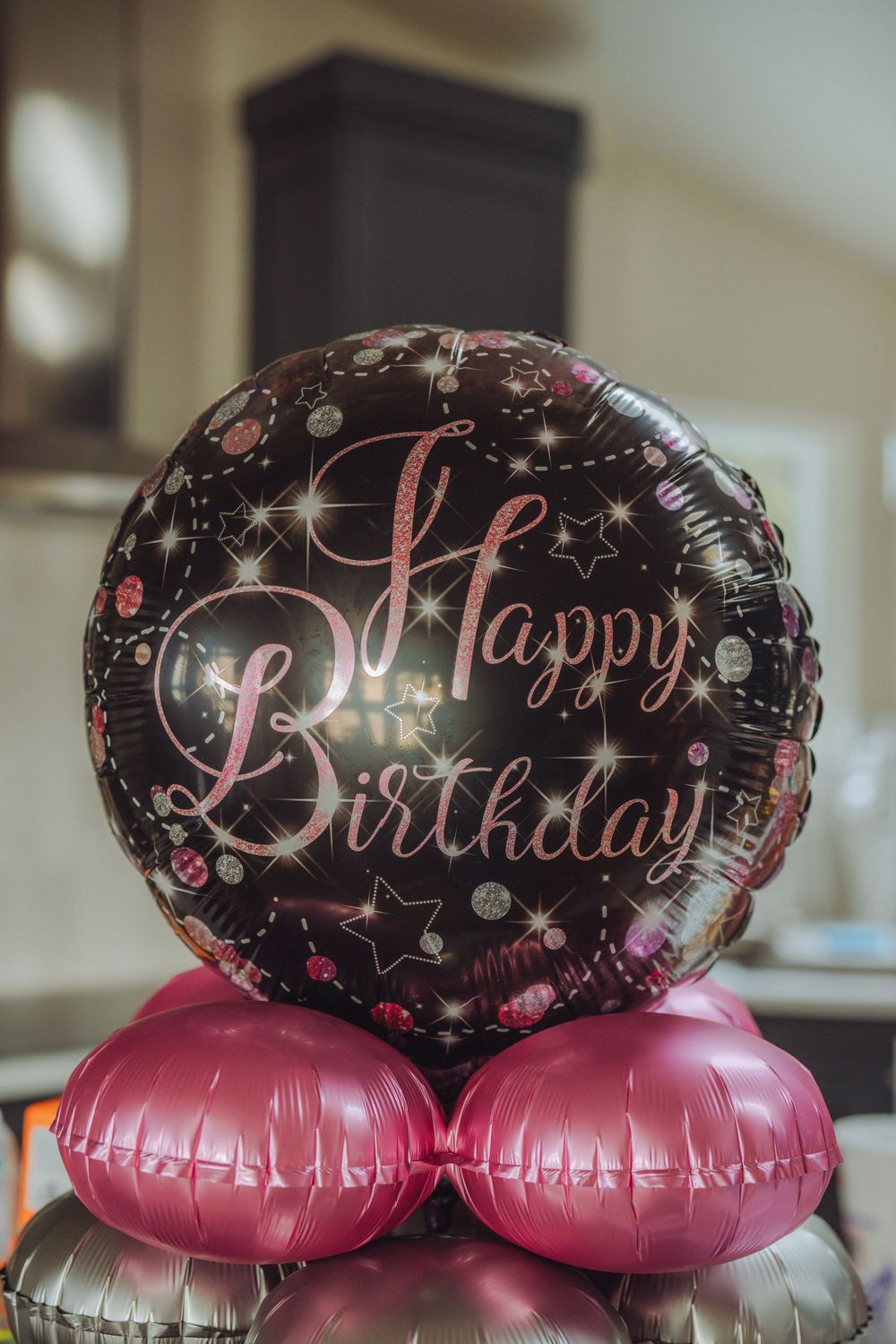 Black and pink Happy Birthday foil balloon with stars and sparkles, sitting on pink and silver balloons.