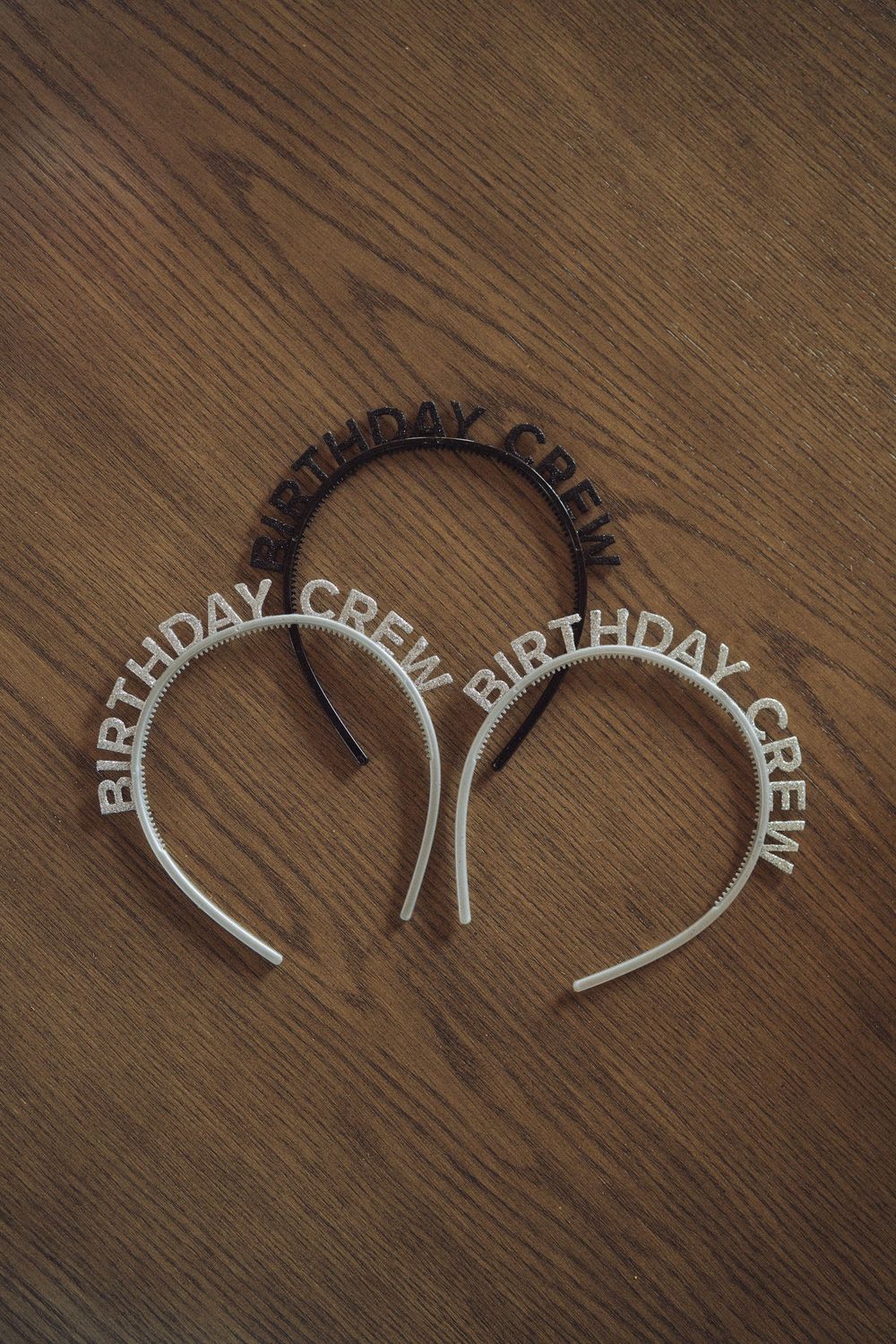Three Birthday Crew headbands in silver and black displayed on a wooden surface, perfect for birthday party accessories.