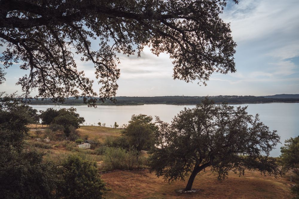 Scenic lakeside view framed by oak trees with calm water and rolling hills under a cloudy sky in Texas.