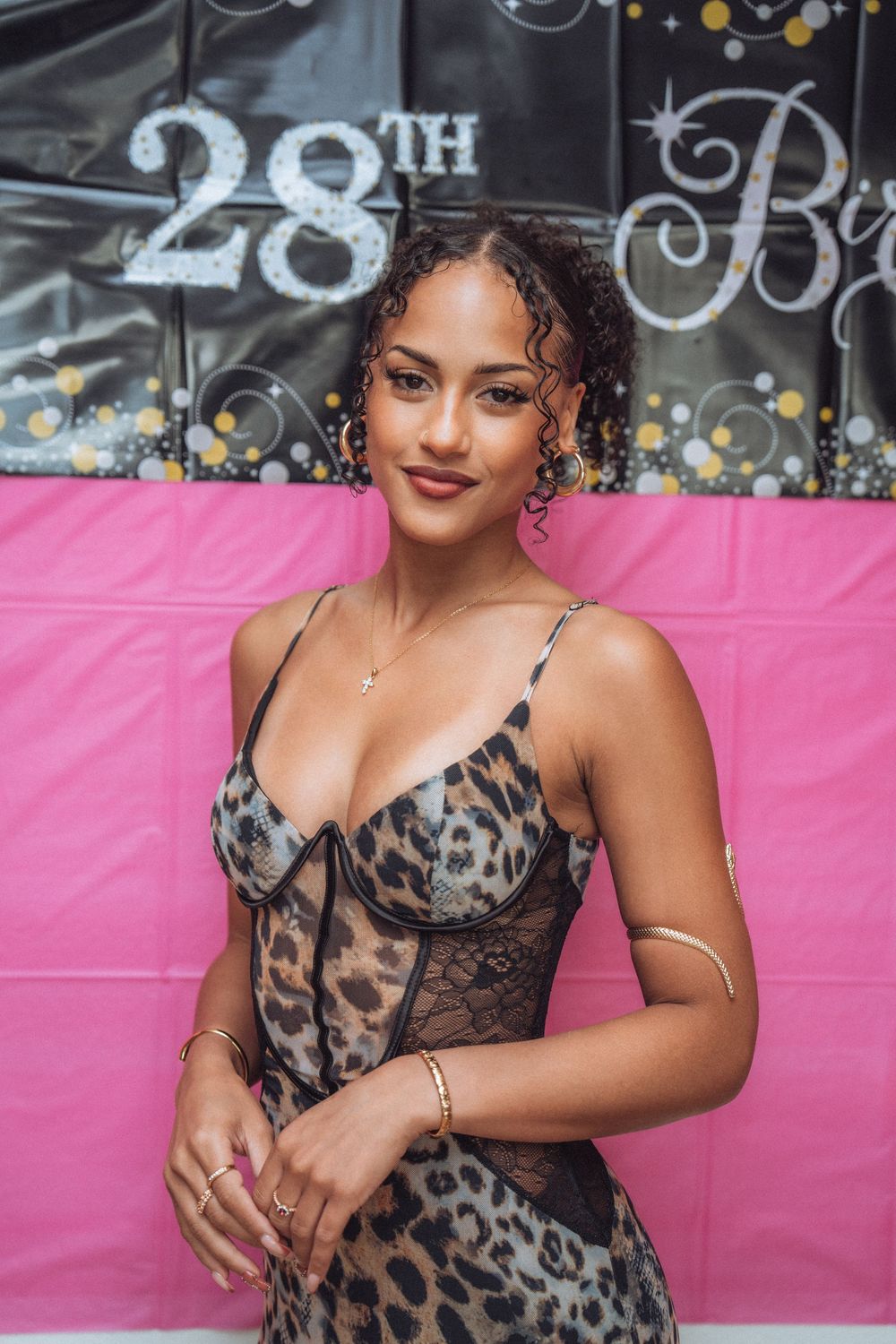 Young woman in leopard print dress poses at a 28th birthday party celebration with pink and black decorations.
