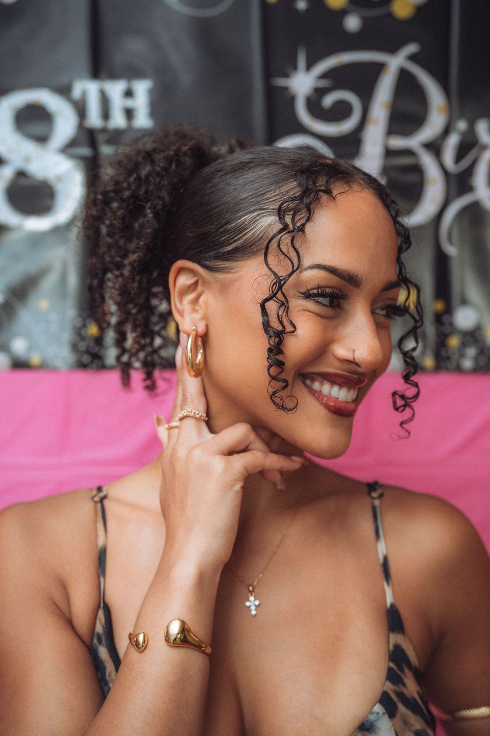 A smiling young woman with curly hair wearing gold jewelry at an 18th birthday party celebration.