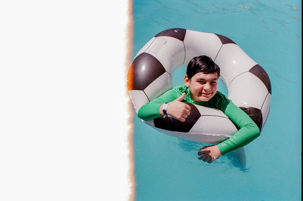 Boy smiling in a soccer ball inflatable ring floating in a bright blue swimming pool.