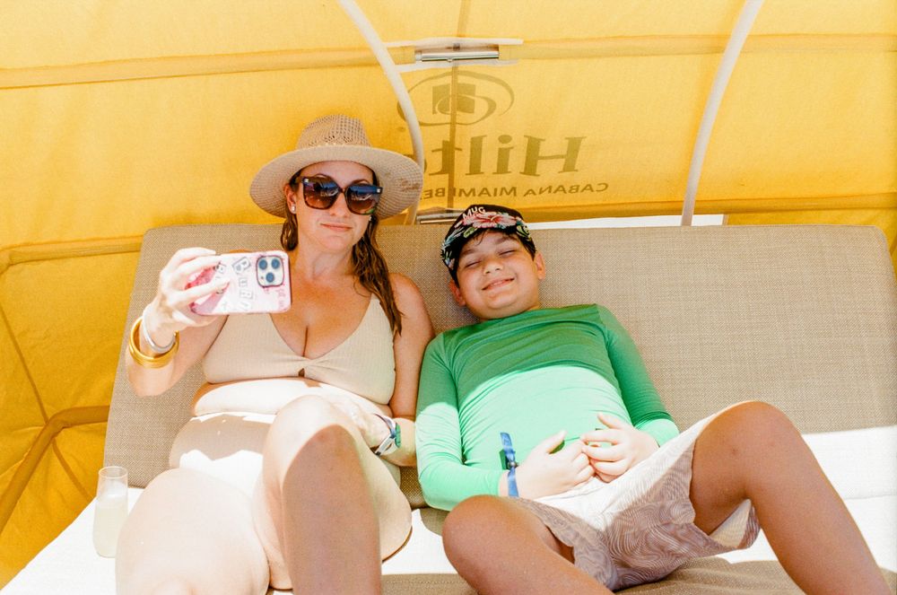 Woman and child taking a selfie while relaxing under a yellow beach cabana at a Hilton resort.