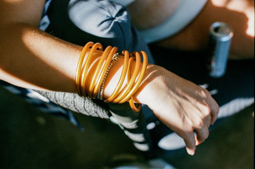 Close-up of a wrist adorned with multiple stacked golden bangles and bracelets in warm sunlight.