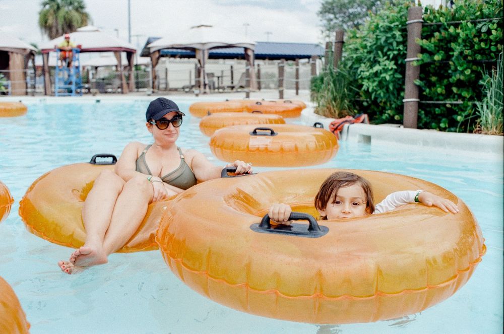 Two people relax on golden inflatable rings in a lazy river at a water park on a sunny day.