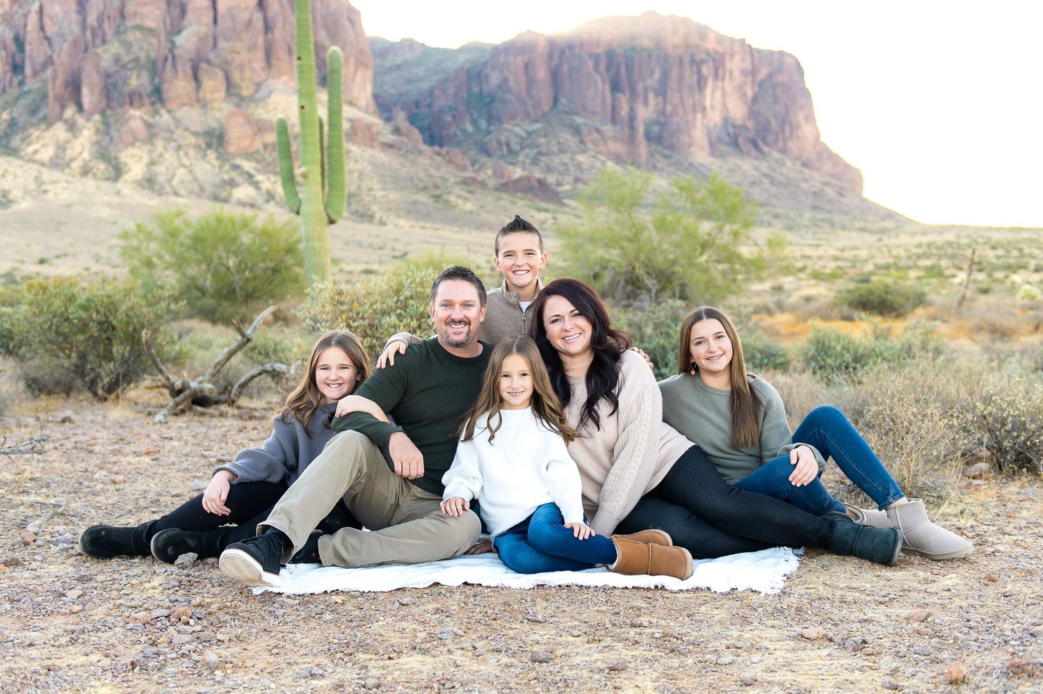 Family of 7 poses together at the foot of the Superstition Mountains at sunrise during their family vacation photo session.