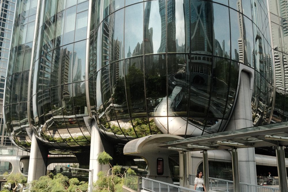 Futuristic glass skyscraper with curved reflective facade mirrors city buildings in a modern urban district.