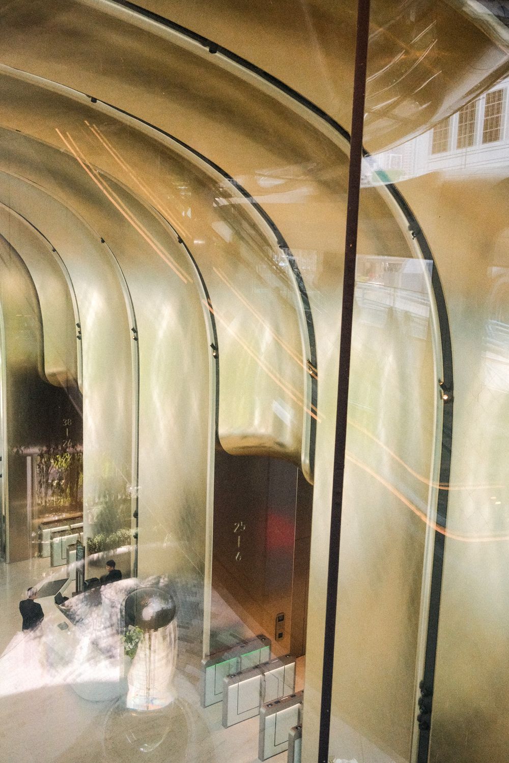 Modern architectural interior with arched glass walls reflecting golden light and contemporary furniture below.
