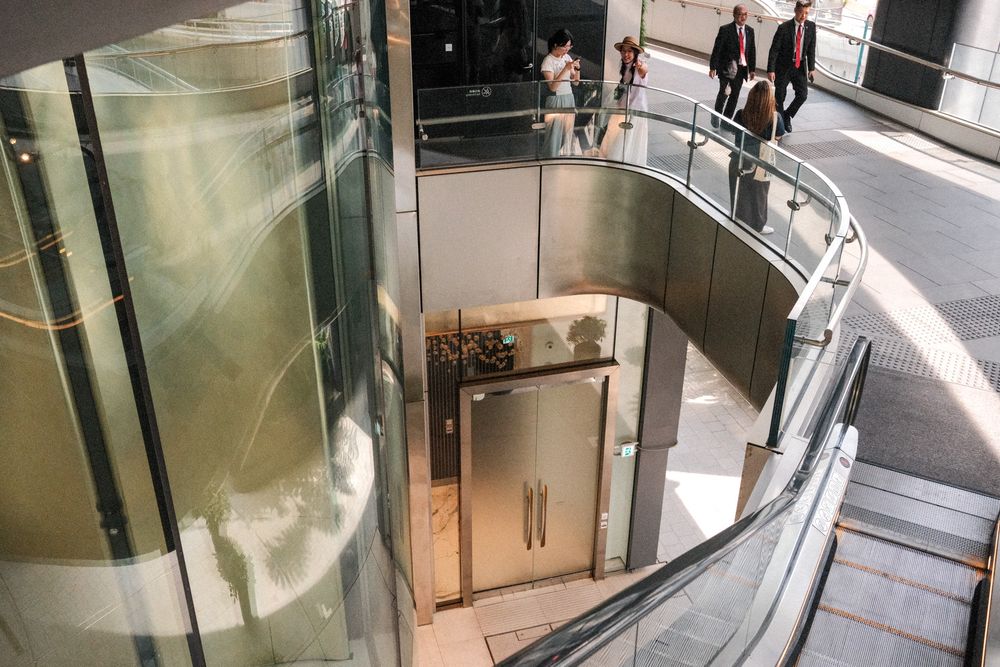 Modern glass elevator shaft with spiral staircase and metal doors in a contemporary building interior.