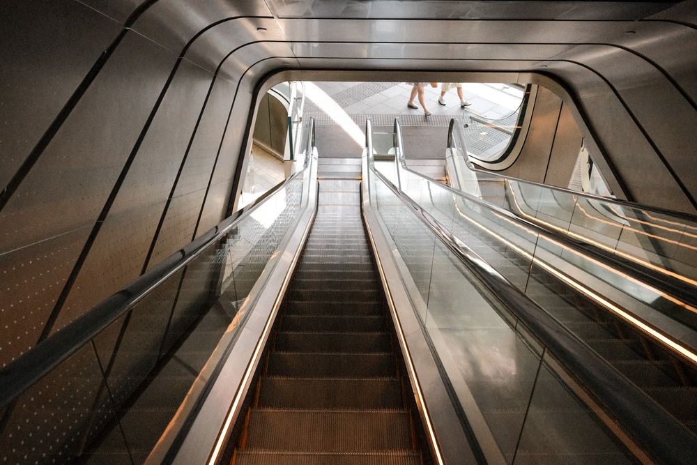 Modern escalator ascending in a sleek subway station with metallic walls and warm lighting.