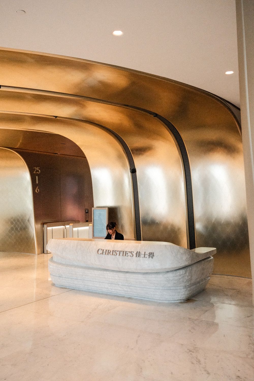 Christie's auction house reception desk with golden curved archway walls and marble counter in elegant lobby.