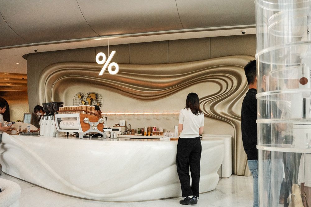 Modern % Arabica coffee shop with sleek white counter, wavy wall design, and minimalist interior decor.
