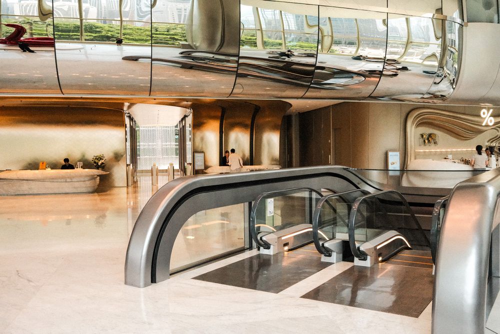 Modern luxury airport terminal interior with sleek metallic escalators, marble floors, and reflective ceiling design.