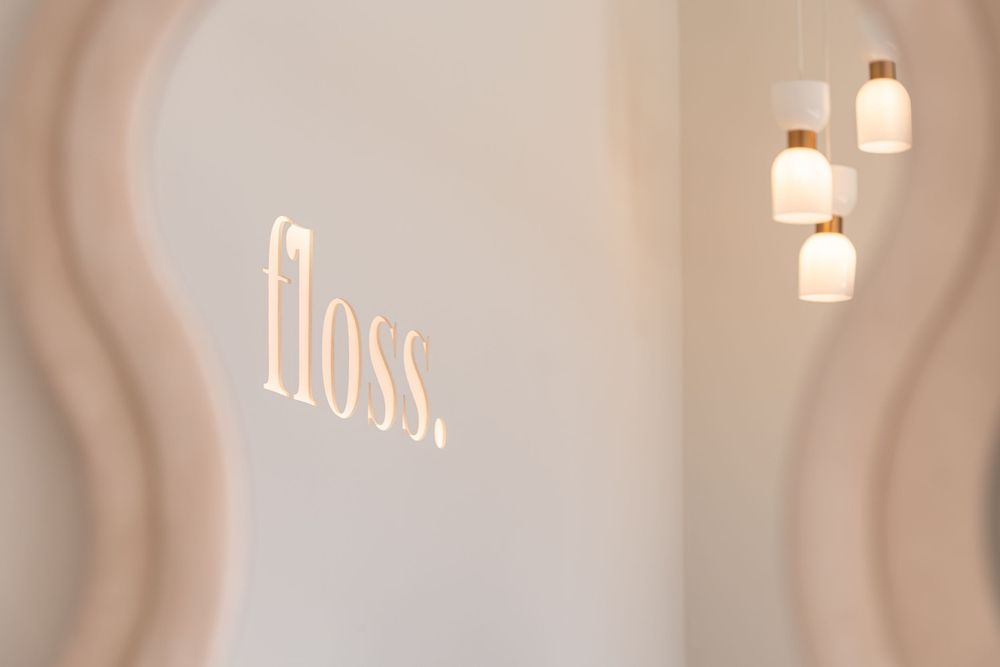Modern dental office wall with glowing 'floss.' logo sign and elegant pendant lights in soft neutral tones.