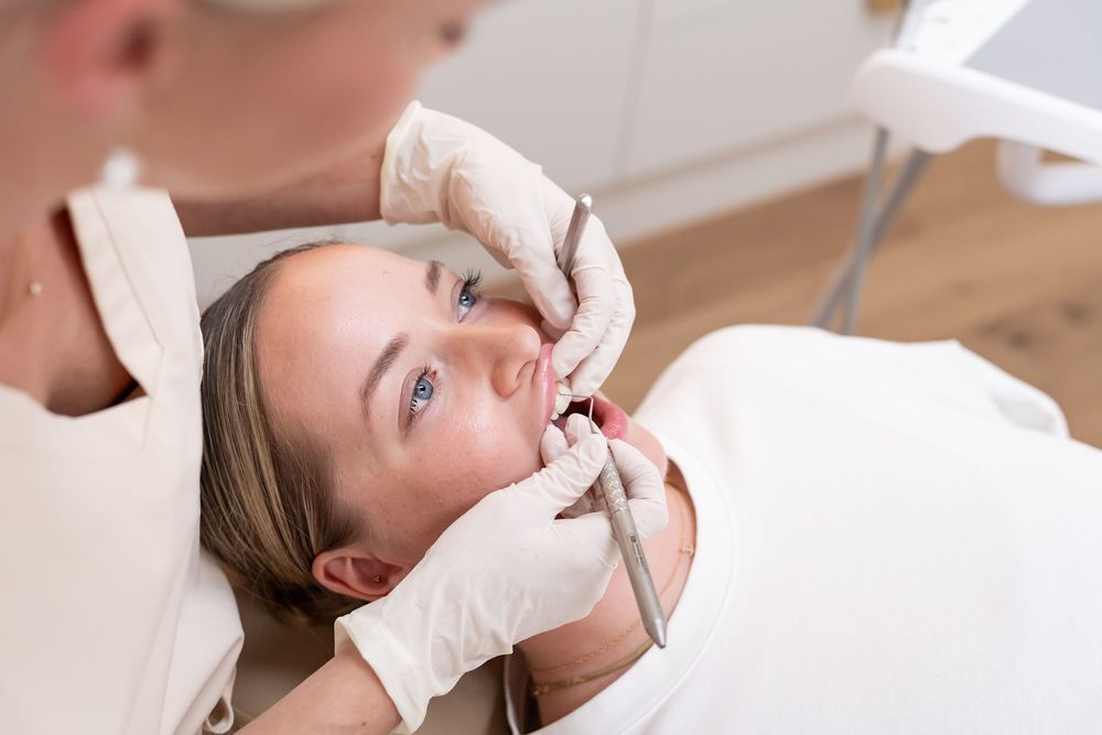 A dentist in gloves performs a dental examination on a young woman lying in a dental chair.