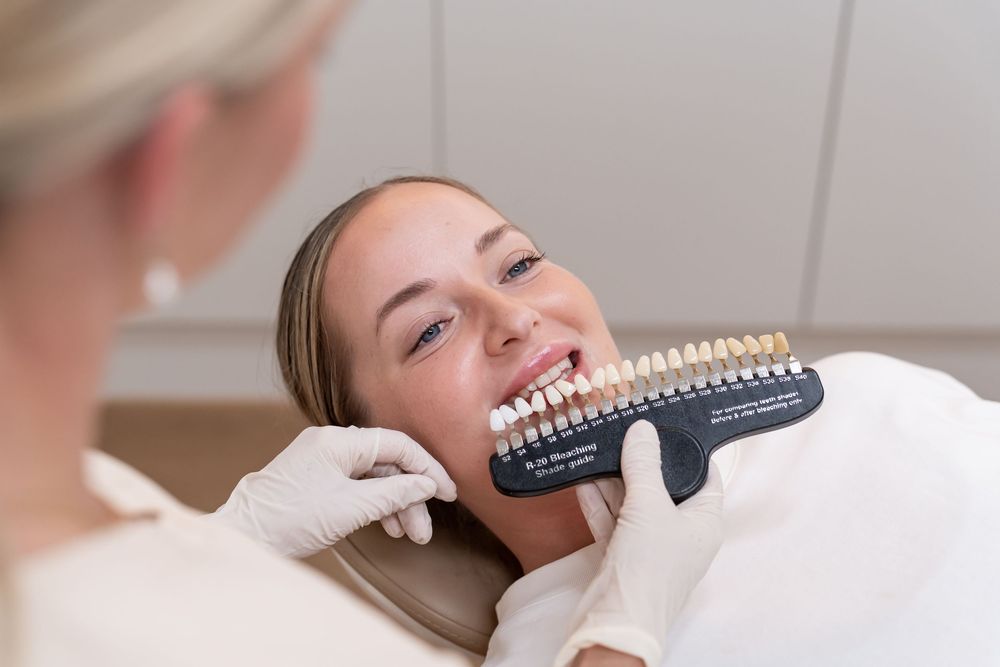 Dentist holding tooth shade guide next to smiling female patient during cosmetic dental consultation.