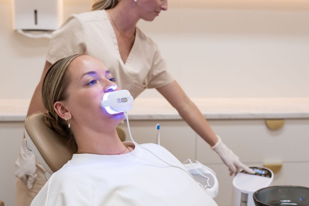Woman receiving professional teeth whitening treatment at dentist office with UV light tray in mouth.