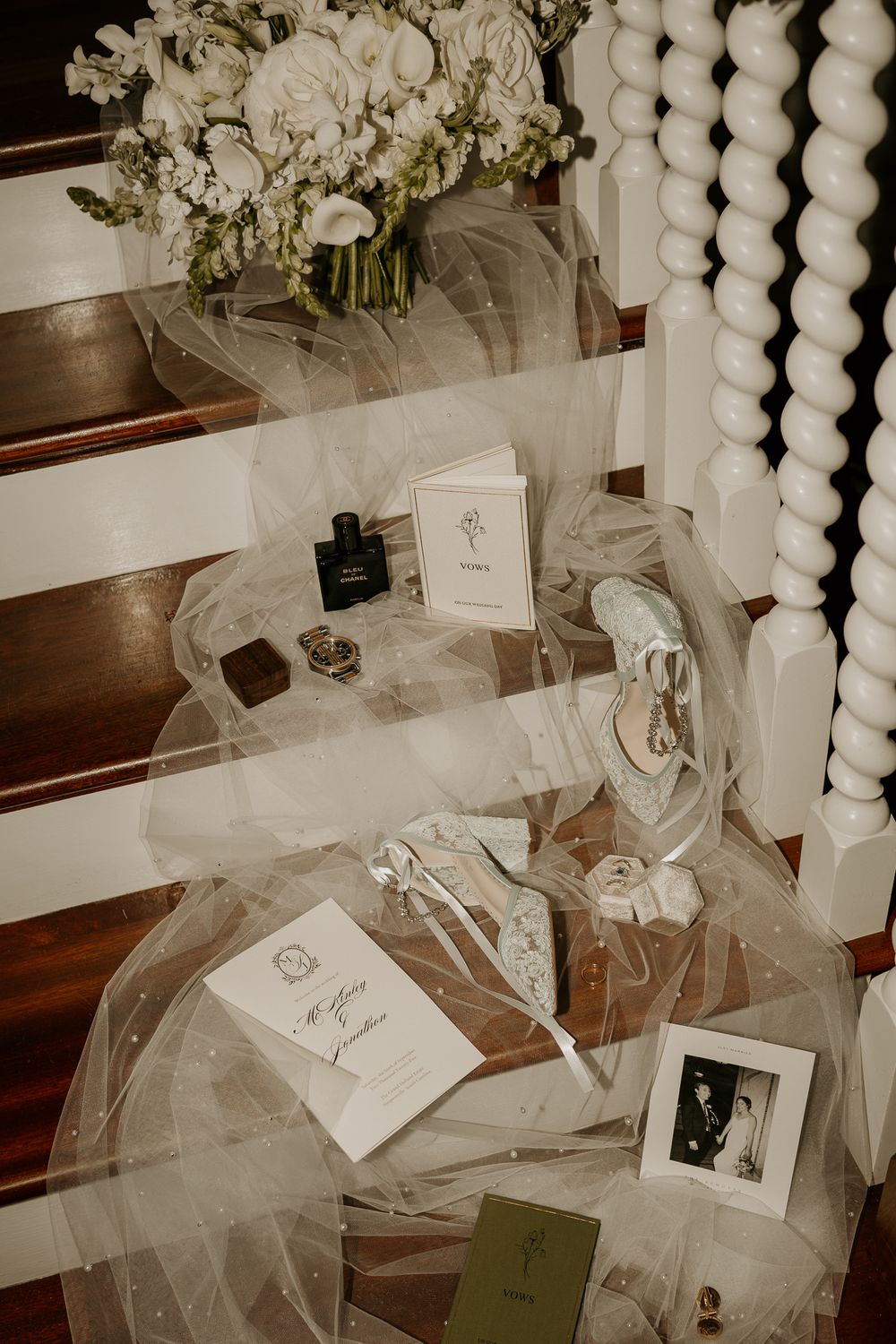 Elegant bridal flat lay featuring veil, heels, bouquet, perfume, and keepsakes on wooden stairs.