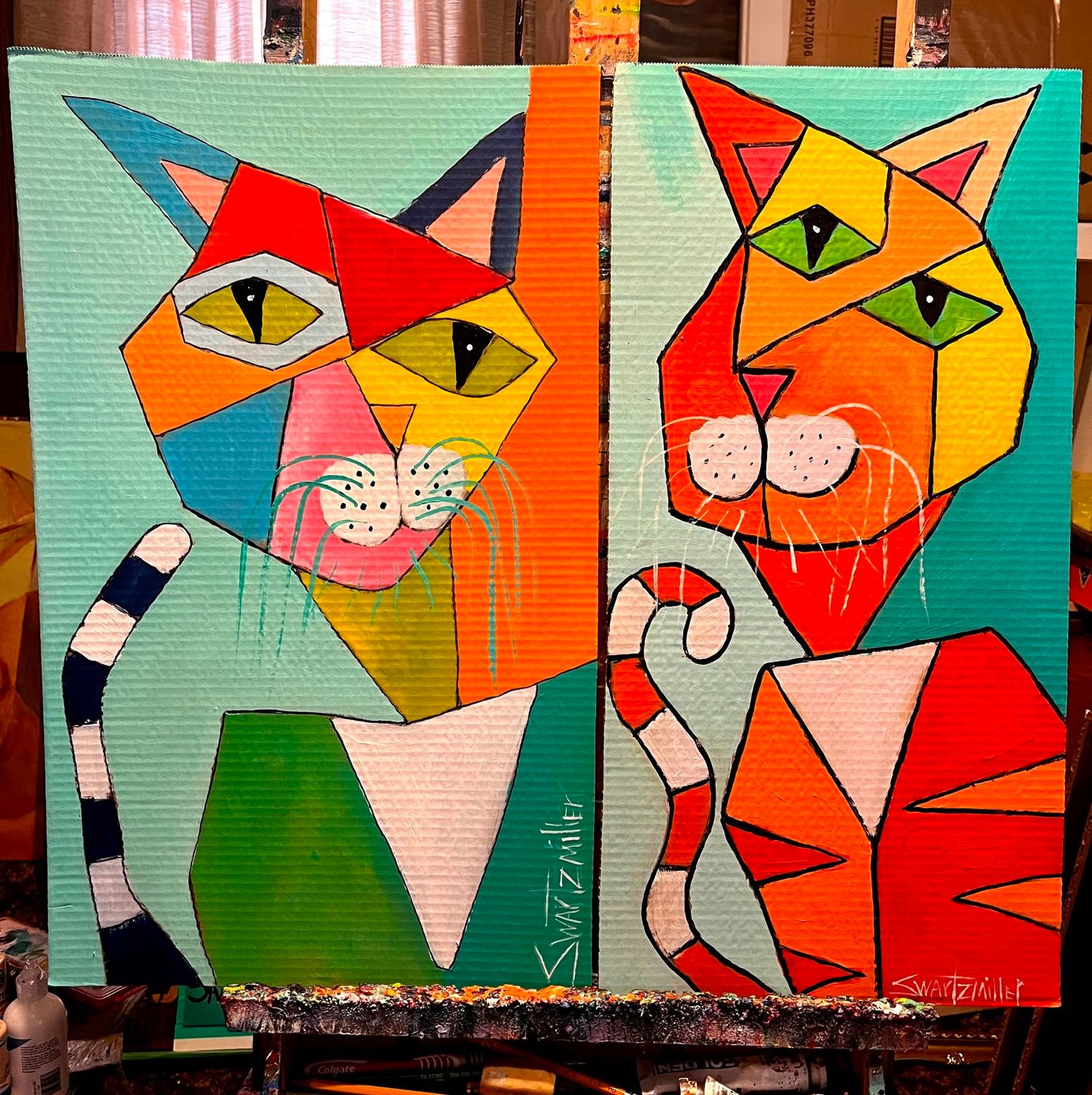 Colorful cubist painting of two cats side by side, featuring bold geometric shapes in vibrant red, orange, blue, and green tones.