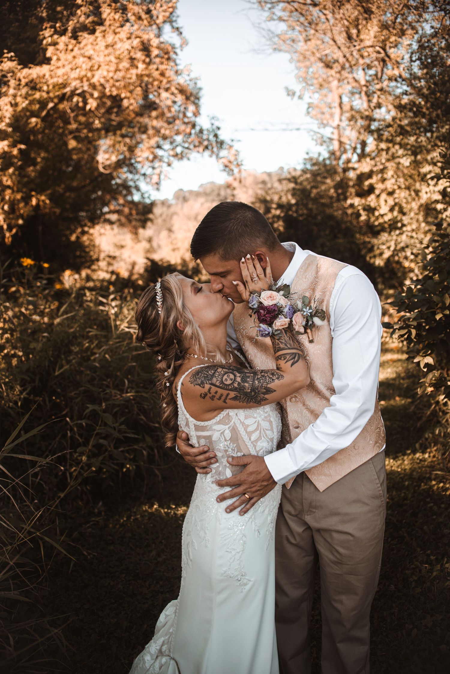 A romantic golden-hour wedding photo shows a couple sharing an intimate kiss among autumn foliage.