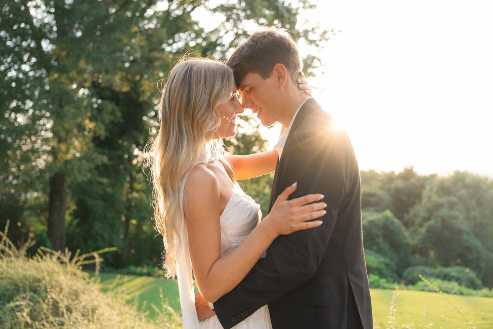 Bride and groom share romantic moment touching foreheads in golden sunset garden light.