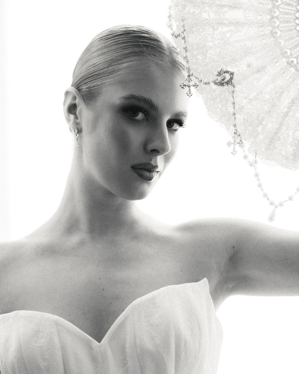 Black and white close-up portrait of blonde bride in strapless gown with ornate beaded veil accessory.
