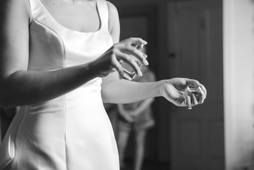 Black and white photo of a bride in a white dress spraying perfume on her wrist.