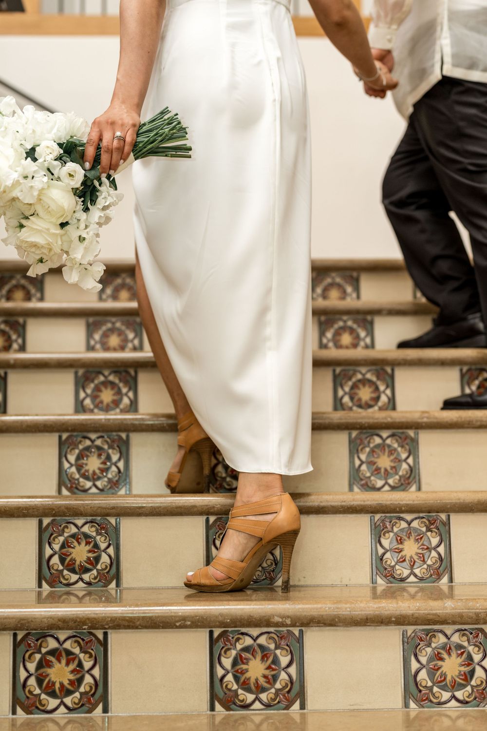 Detail shot of bride's white dress and shoes on decorative tiled stairs with bouquet.