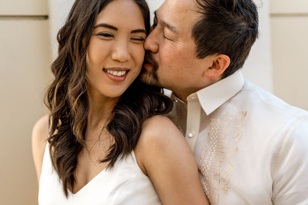 Intimate moment of affection between romantic couple dressed in light colors against neutral background.