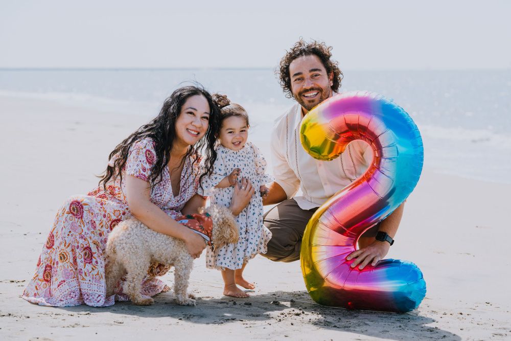 Family beach photo with colorful number 2 balloon and pet dog.