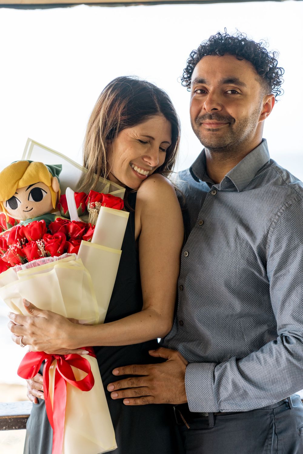 Couple sharing romantic moment while holding gift bouquet with plush toy.