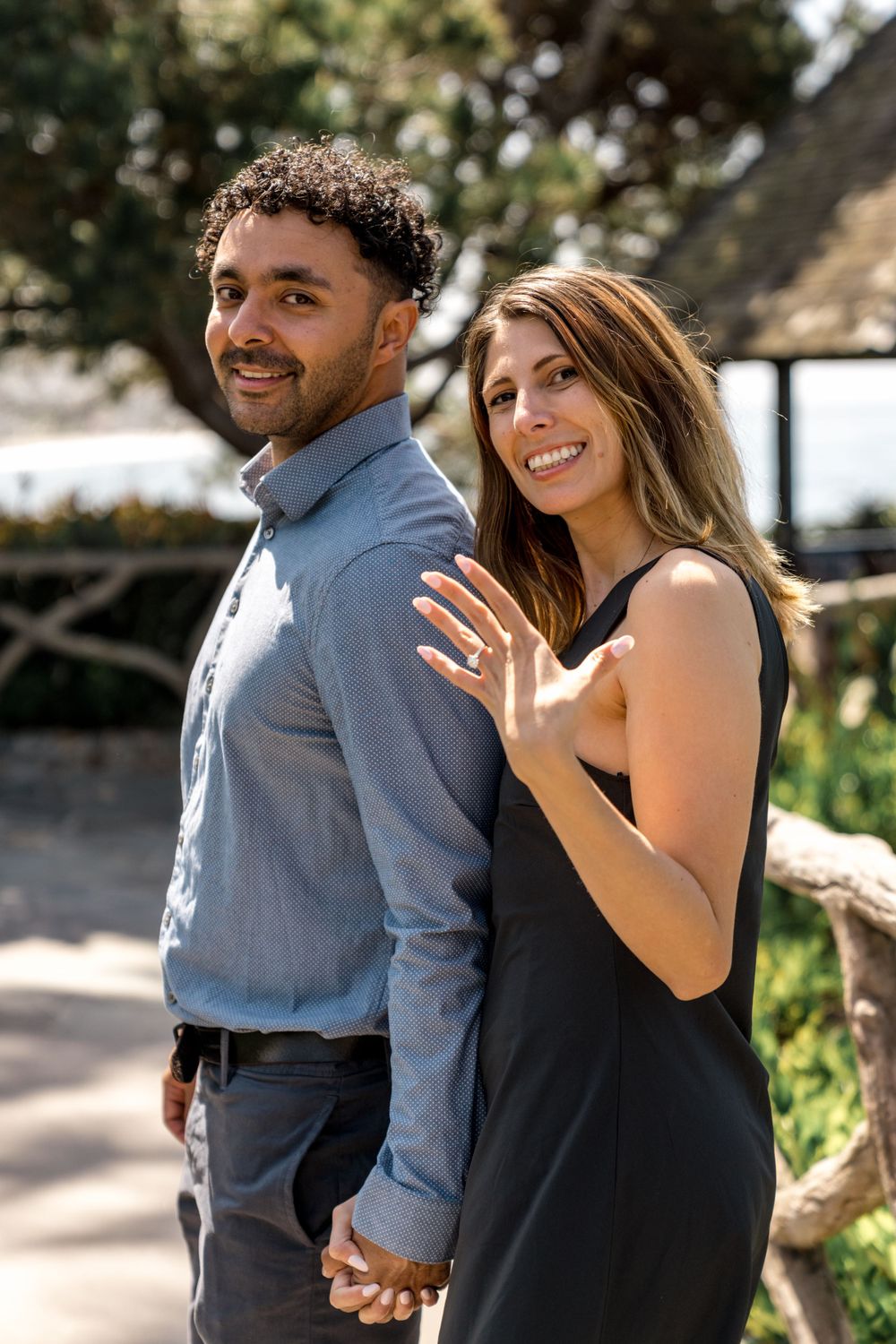 Happy engaged couple posing outdoors with woman showing off ring.