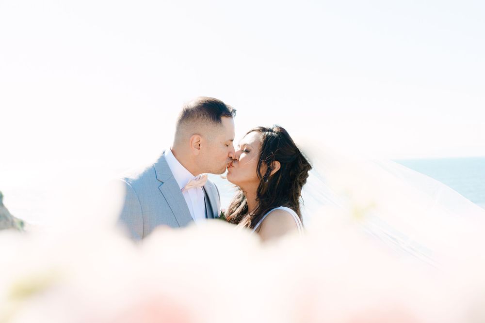Romantic seaside photo of couple sharing a kiss with soft dreamy lighting.
