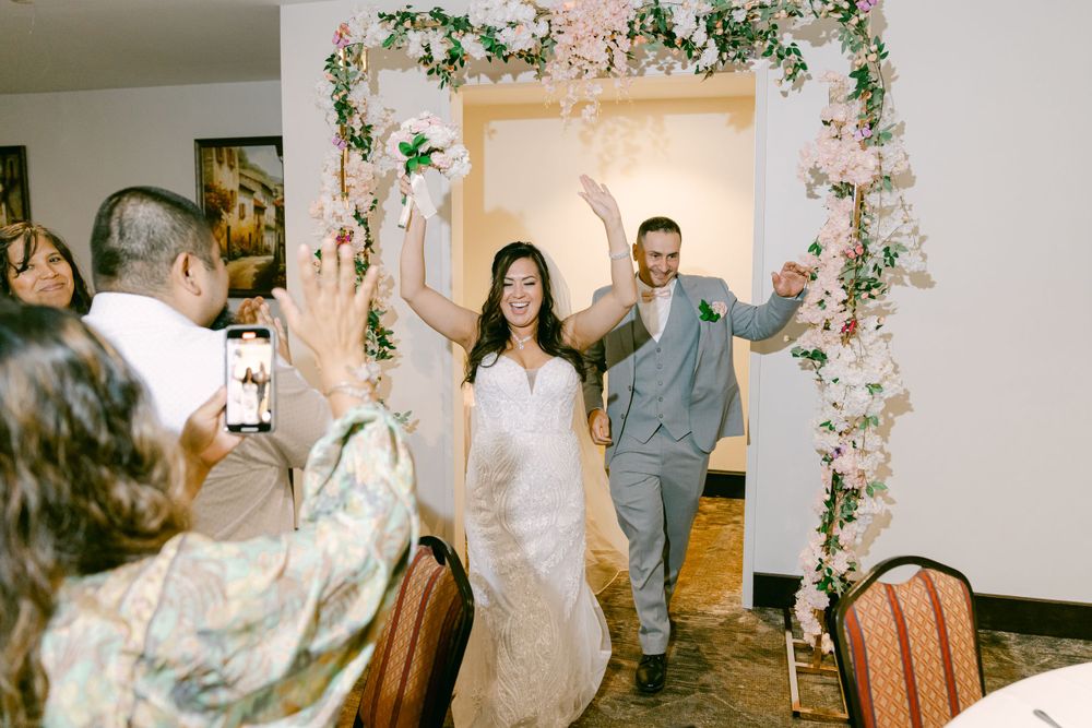 Wedding celebration with newlyweds entering under floral arch as guests cheer.
