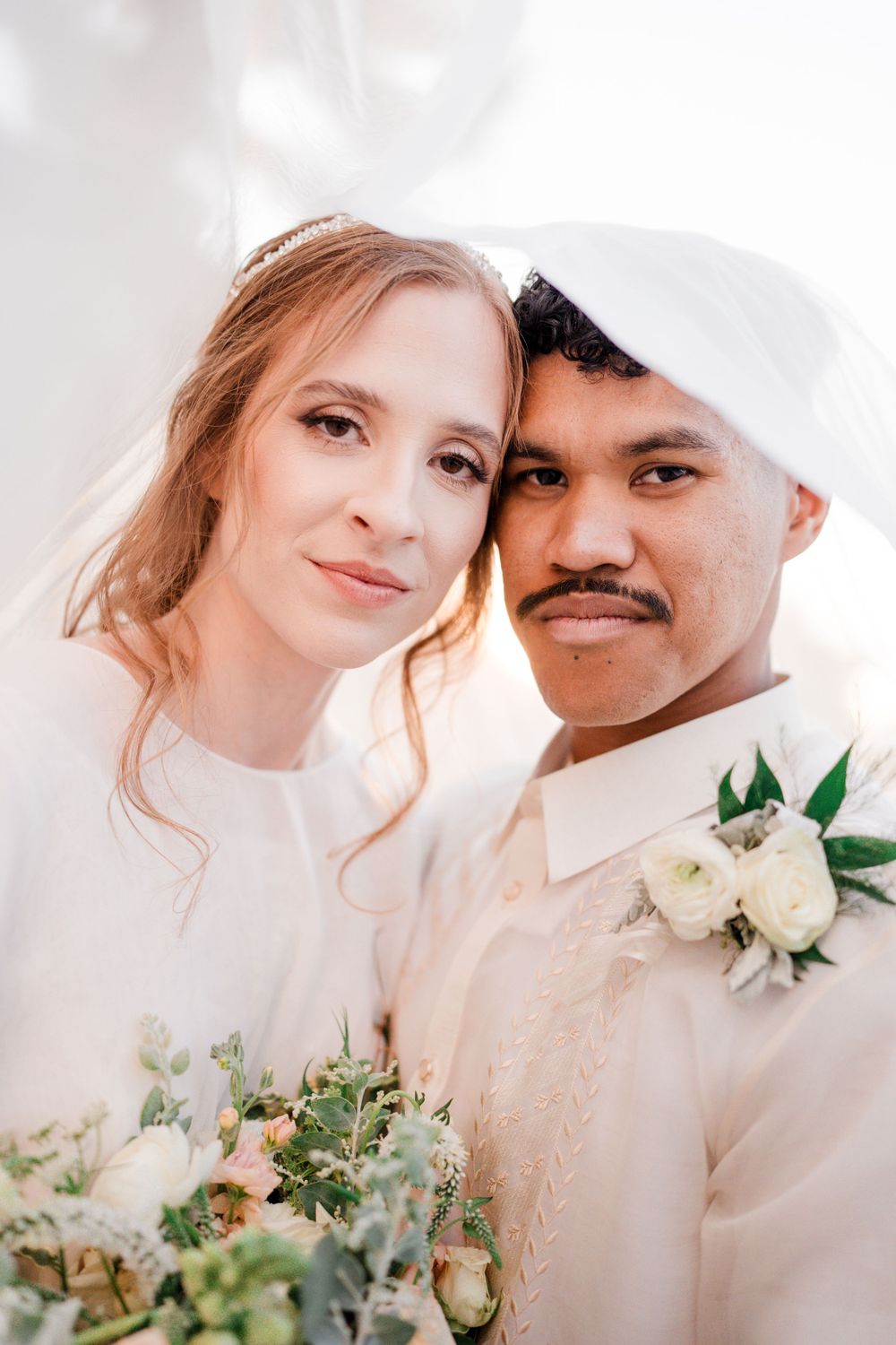 Wedding portrait of couple in white attire with floral bouquet.