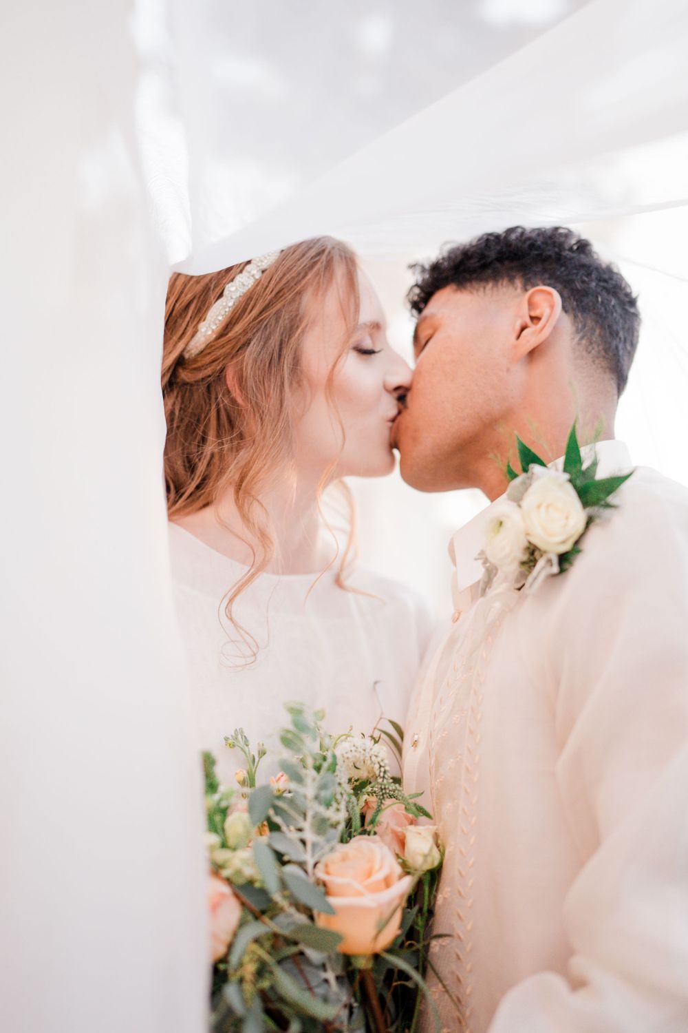 Romantic wedding kiss between couple with white roses and soft lighting.