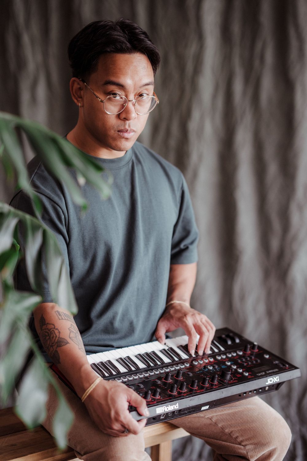 Musician with glasses working on MIDI keyboard controller in home studio setting.