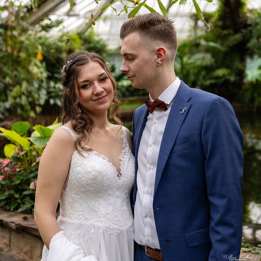 A couple poses together in a lush greenhouse setting during their wedding.