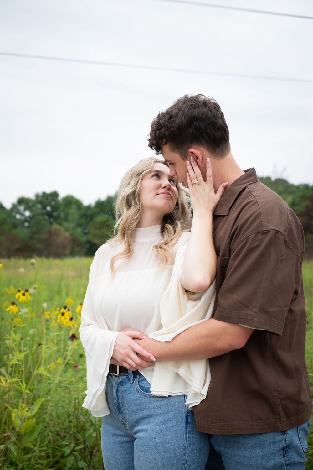 A couple shares a tender moment in a wildflower field, woman in white top touching mans face.