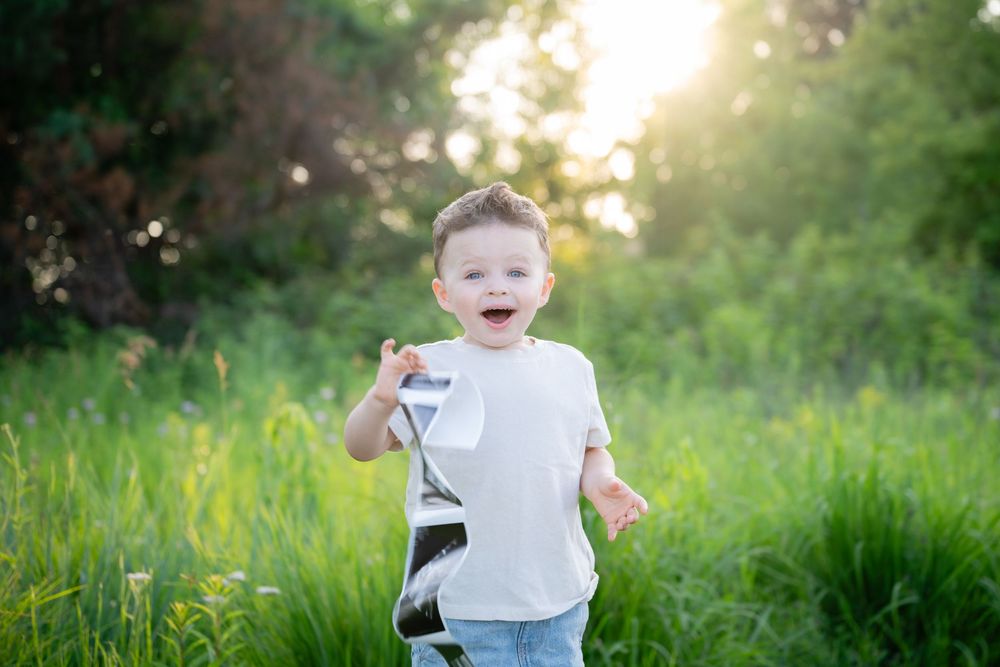 Happy toddler boy laughing and running in a lush green field on a sunny day.
