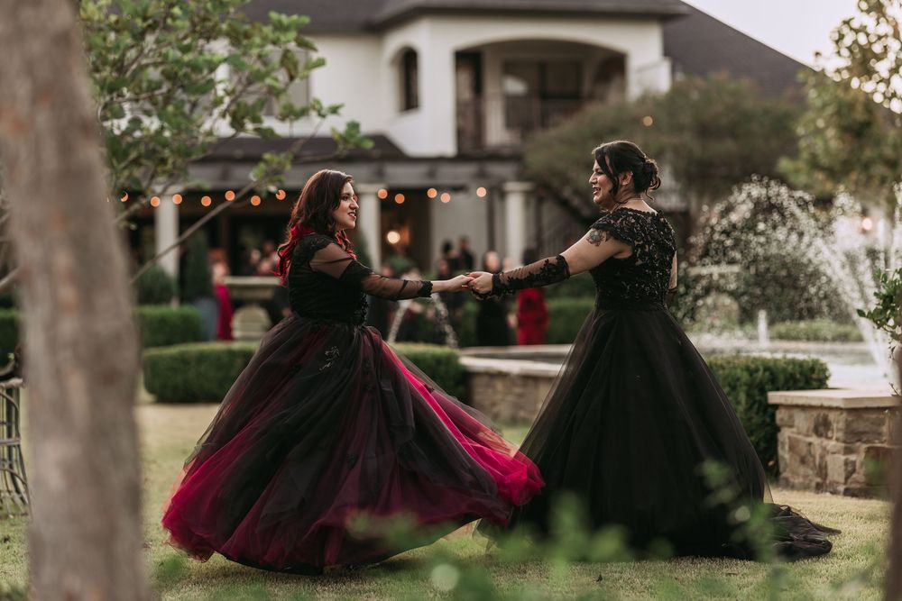 A couple in formal attire dances together outdoors in a romantic garden setting at sunset.