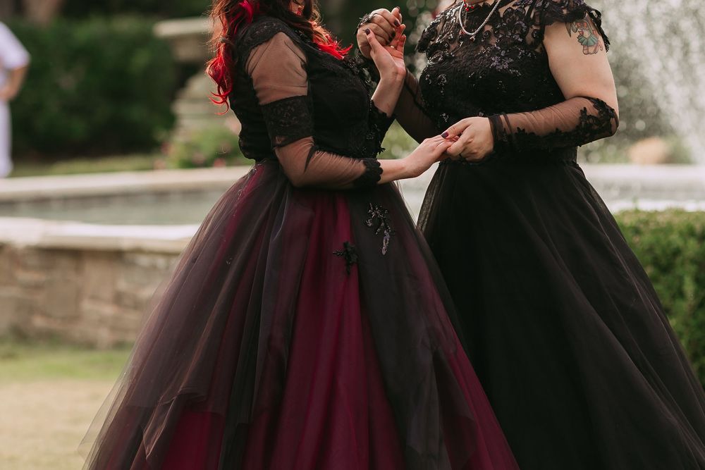 Wedding party wearing elegant black and burgundy dresses poses together outdoors.